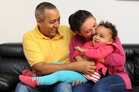 Mutter, Vater und Kind in liebevoller Umarmung auf eine Couc