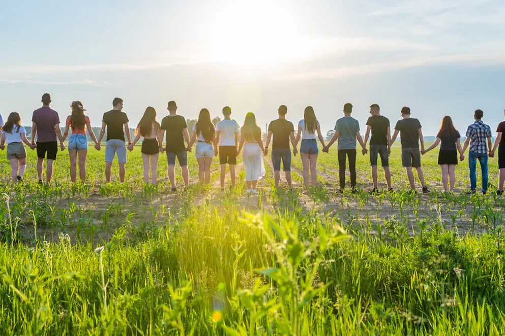 Eine Menschen-Kette von hinten auf einem grünen Feld. Die Menschen halten sich an den Händen.